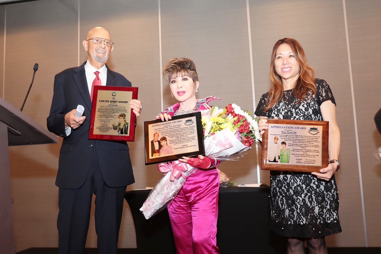Award recipients holding plaques and flowers on stage
